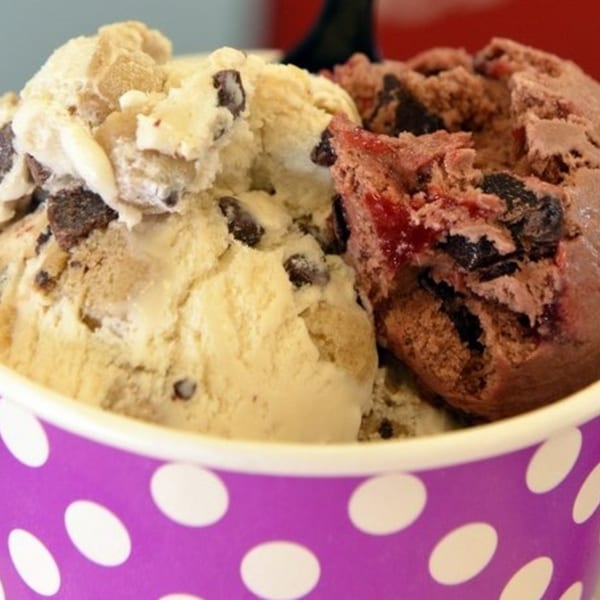 Two scoops of ice cream, one vanilla with chocolate chips and one chocolate with cherries, in a polka dot cup.