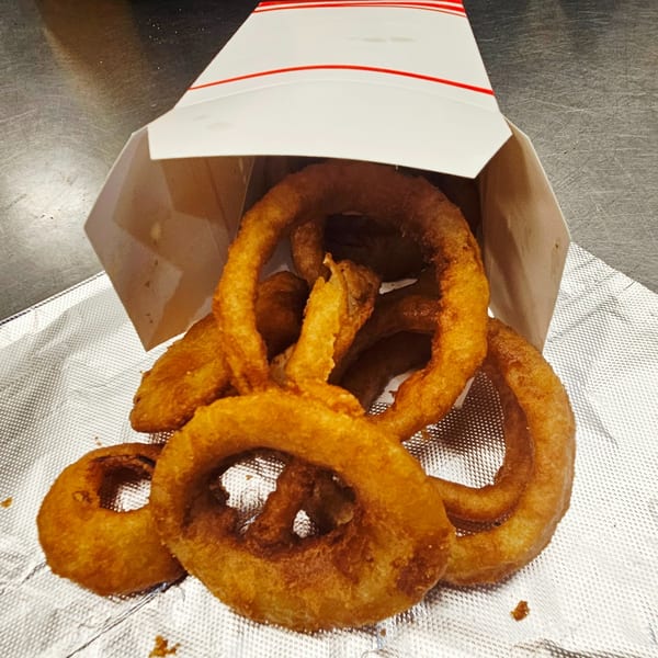 Golden-brown onion rings spilling out of a white and red striped paper container onto foil.