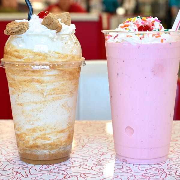 Two Classic Burgers milkshakes, one caramel and one strawberry, topped with whipped cream and sprinkles.
