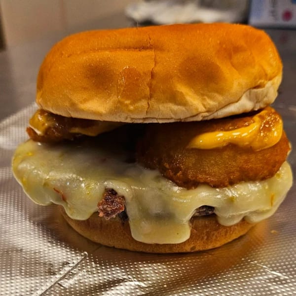 Classic Burgers' cheeseburger with melted white cheese, onion rings, and a drizzle of orange sauce.
